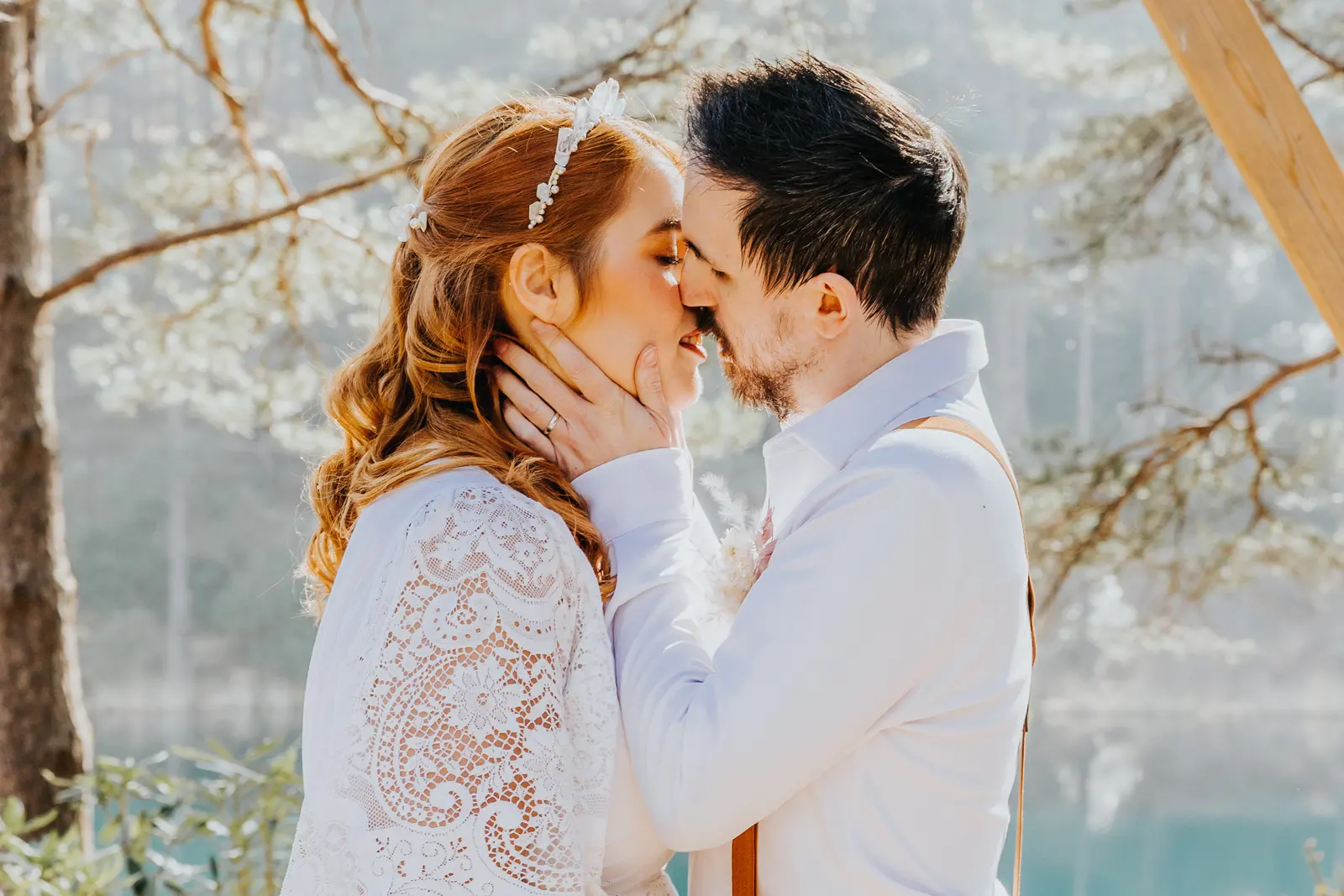 A couple kiss beneath the hexagonal arch, the turquoise lake and pines behind them.
