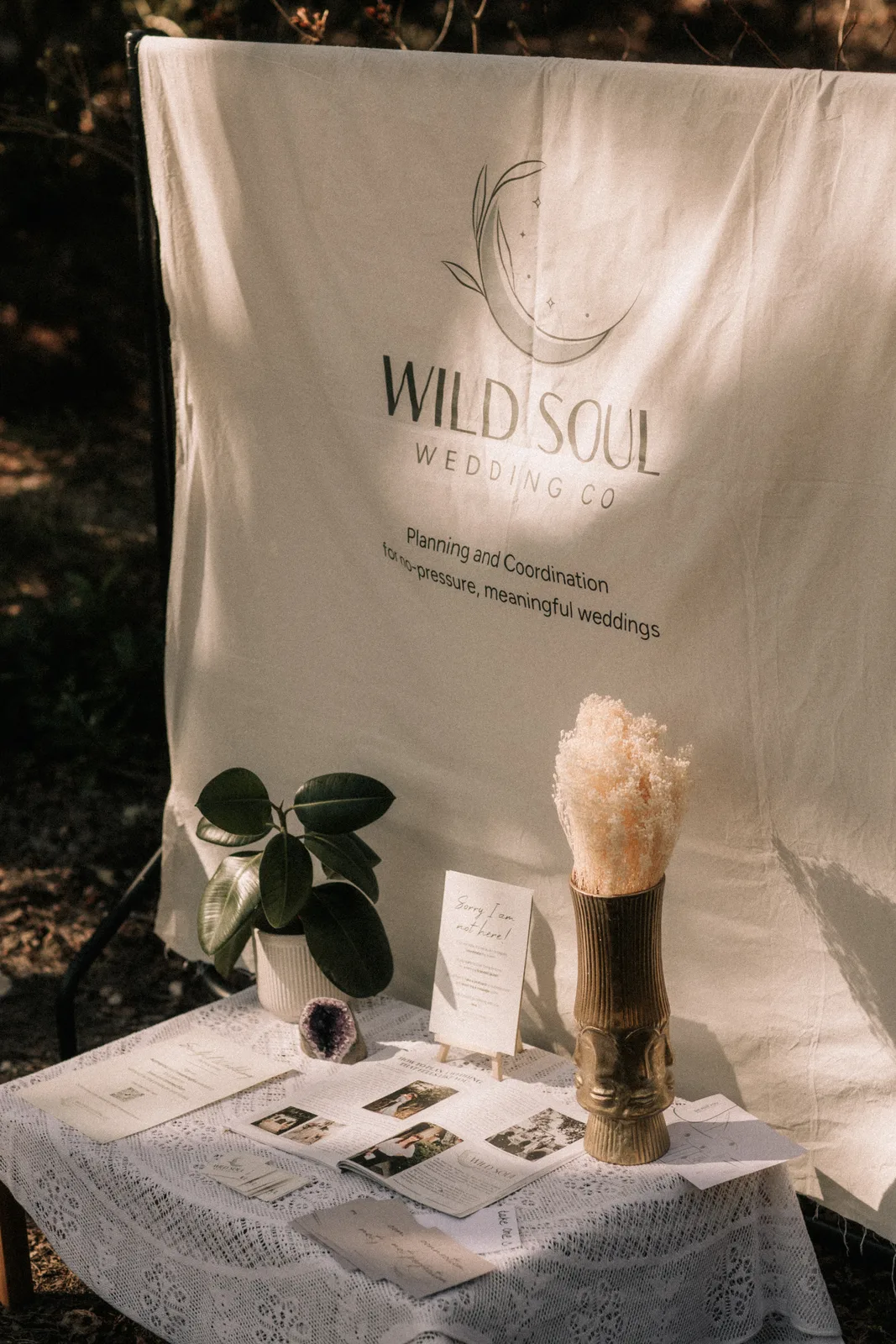 A linen banner reading Wild Soul Wedding Co hangs behind a small table with pampas in a vase.