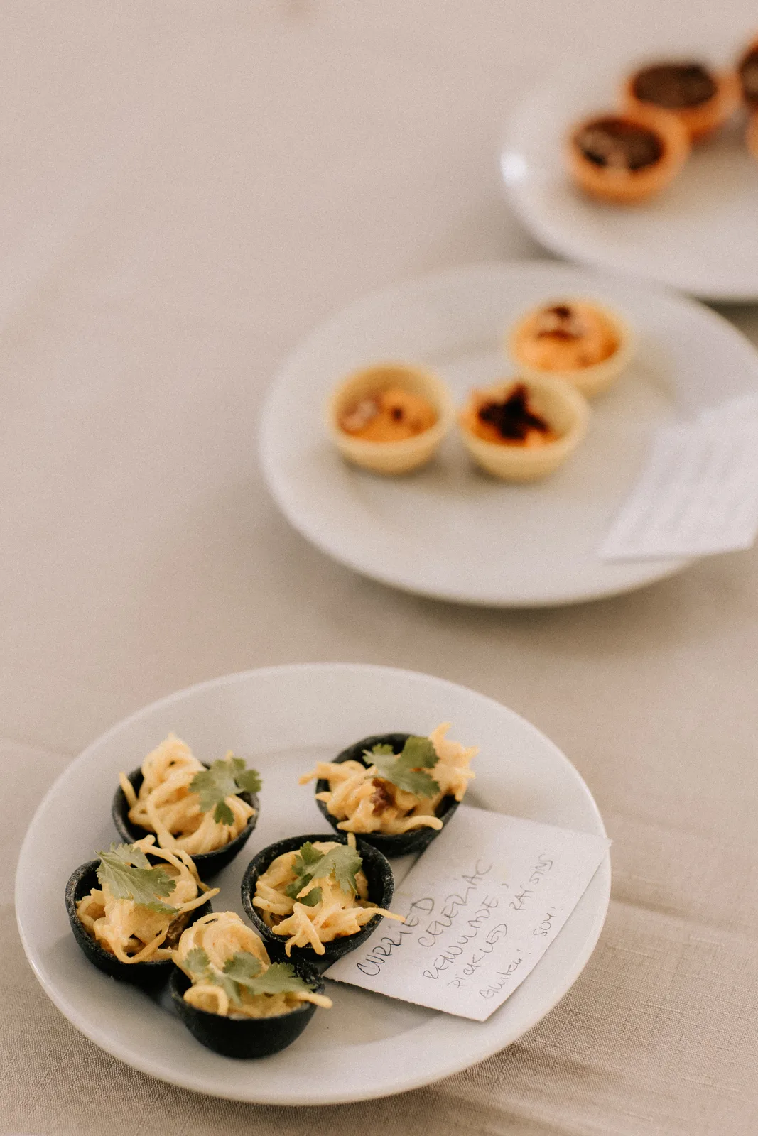 Two plates of small tarts and canapés on a white cloth.